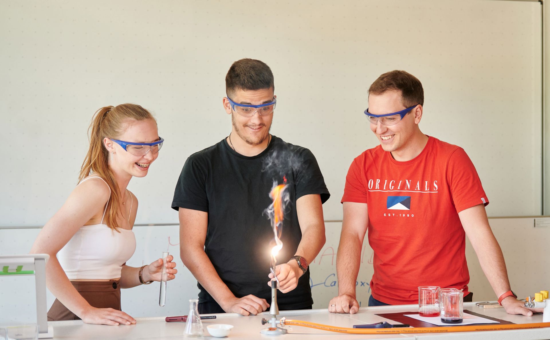 Eine Schülerin und ein Schüler führen mit ihrem Lehrer ein Experiment im Chemie-Unterricht durch.